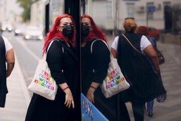 Wall Mural - European plus size woman gets on the bus in face mask. Young red pink haired body positive girl.