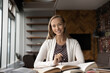 © fizkes - Portrait of smiling millennial female student study with books prepare for examination. Happy smart young Caucasian woman sit at desk read textbooks write make notes. Distant education concept.