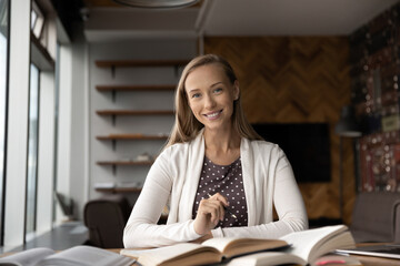 Portrait of smiling millennial female student study with books prepare for examination. Happy smart young Caucasian woman sit at desk read textbooks write make notes. Distant education concept.