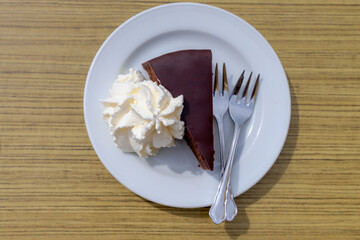 Top view of Original Sacher-Torte on table served with whipping cream, The cake consists of a dense chocolate cake with a thin layer coated in dark chocolate icing on the top, Famous cake in Austria.