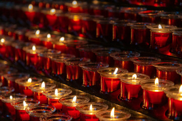 Selective focus of offering of red candles inside the church, Burning wax candlelight in the dark, Flame with warm light tone with black background.