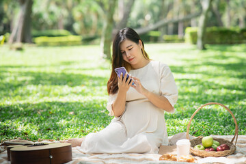 Wall Mural - The beautiful pregnant woman on picnic and using mobile phone in the garden