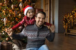 Smiling sincere young father playing plane with adorable small preschool kid son, spending relaxed holiday family time together near decorated festive evergreen Christmas tree in designed living room.