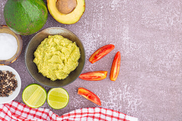 Wall Mural - Organic avocado with seed, avocado halves, whole fruit, and fresh guacamole in a bowl with salt and pepper on a small dish on gray stone background. Top view. Concept of healthy fruit