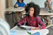 © insta_photos - Happy African American schoolgirl looking listening to teacher using tablet device sitting in classroom with group of schoolchildren using laptop computers. Modern technologies for education concept.