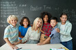 © insta_photos - Portrait of cheerful smiling teacher and diverse schoolchildren standing posing on chalkboard blackboard background looking at camera happy after school reopen on mathematics lesson. Diversity.