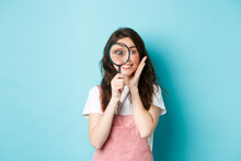 Girl Searching For You. Cute Smiling Woman Recruiter Look Through Magnifying Glass, Staring At Camera, Investigating, Looking For Someone, Standing Over Blue Background