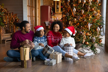 Wall Mural - Smiling young African American family with small children unpack boxes with New Year gifts together. Happy biracial parents with kids open gifts presents on Christmas morning. Winter holiday concept.