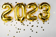 golden foil balloon 2023 New Year. Numbers two thousand twenty three from a foil figure on a gray cement background. Golden confetti and celebration.