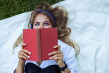 Cute Attractive Woman Reading Book While Lying On Blanket On Grass