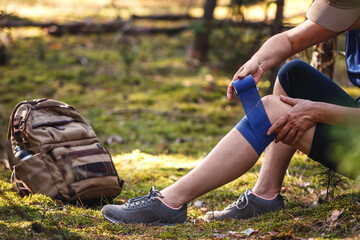 Injured hiker putting elastic bandage to her knee. Accident during hiking. Trekking first aid. Knee joint pain and tendon problems during adventure in nature