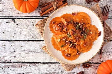 Sticker - Pumpkin filled ravioli pasta with nuts and pumpkin seeds. Above view on a rustic white wood background. Copy space.