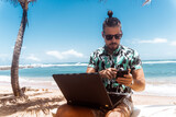 Fototapeta Fototapety z morzem do Twojej sypialni - Cyfrowy nomada, mężczyzna pracujący na tropikalnej plaży z laptopem i telefonem.