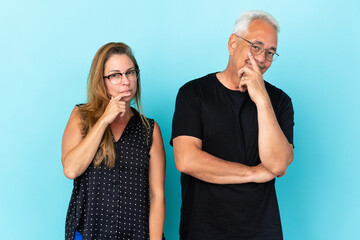 Middle age couple isolated on blue background having doubts and with confuse face expression