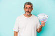Middle age caucasian man holding bills isolated on blue background  confused, feels doubtful and unsure.