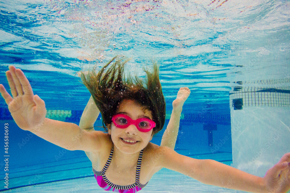 Girl underwater in swimming pool wearing goggles looking at camera ...