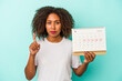 © Asier - Young african american woman holding a calendar isolated on blue background showing number one with finger.