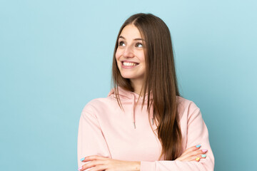 Sticker - Young caucasian woman isolated on blue background looking up while smiling