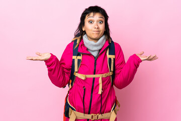 Wall Mural - Young mountaineer girl with a big backpack over isolated pink background having doubts with confuse face expression