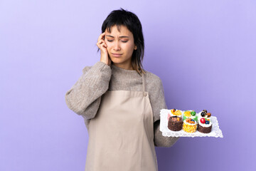Wall Mural - Young Uruguayan woman holding lots of different mini cakes over isolated purple background unhappy and frustrated with something. Negative facial expression