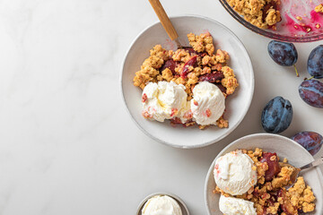 Wall Mural - Fruit crumble. Plum crumble pie with vanilla ice cream in plates with spoons on white marble table for tasty breakfast. Top view