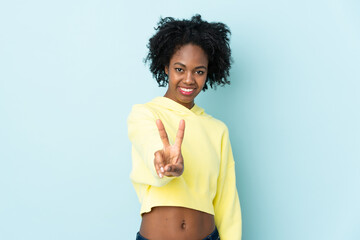 Young African American woman isolated on blue background smiling and showing victory sign