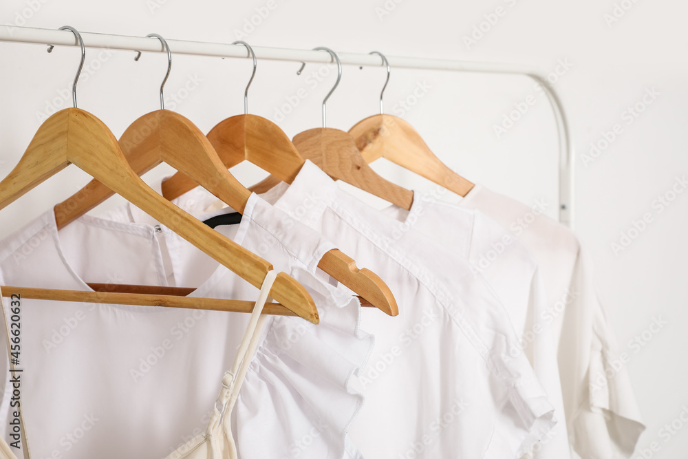 Rack with stylish clothes near light wall, closeup