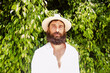 © javiemebravo - young man with beard and long hair wears hat and white shirt surrounded by greenery