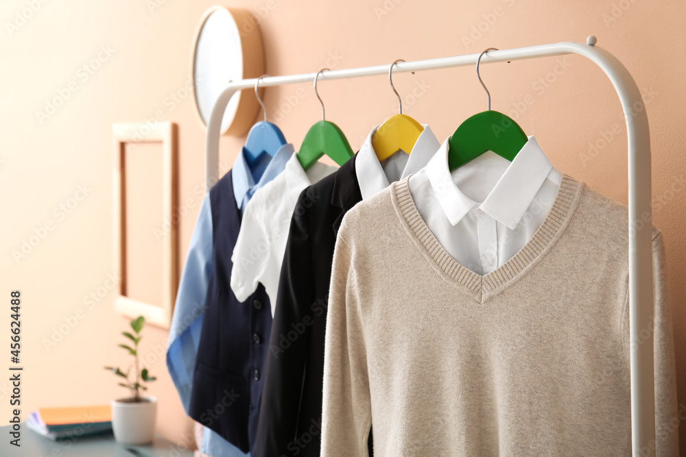 Rack with stylish school uniform near color wall