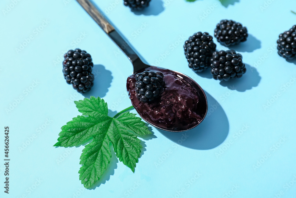 Spoon with tasty blackberry jam and berries on color background