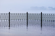 The Fence Of The City Embankment During Flooding With Water And Fog.