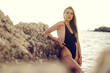 Young beautiful sexy female model in black bikini standing in sea near huge rock
