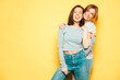 © halayalex - Two young beautiful smiling hipster female in trendy summer white t-shirt and jeans clothes.Sexy carefree women posing near yellow wall in studio.Positive and cheerful models. Shows tongue