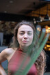 © PIXbank - Young european girl with curly hair with restaurant behind and palm leaf in front