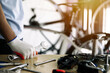 © Deemerwha studio - close - up of the male mechanic working in the bicycle repair shop, mechanic repairing bike using a special tool, wearing protective gloves. Bike Maintenance Concept.