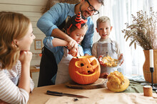 Father Helping  Daughter To Remove Pulp From From Pumpkin While Carving Jack O Lantern With Family