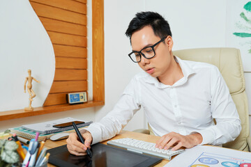 Wall Mural - concentrated young designer using digital pen and graphic tablet when drawing logotype for customer