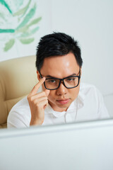 Wall Mural - frowning serious graphic designer adjusting glasses when reading project technical requirements on c