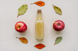 Frischer Apfelsaft in einer Glas Flasche umrahmt von bunten Herbstblättern auf einem beigen Hintergrund. Draufsicht. 