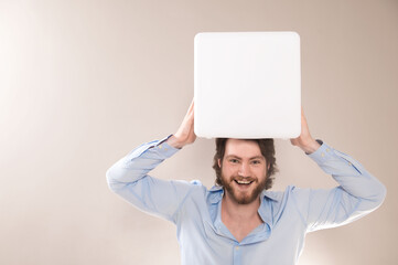 Young attractive man  holding white cube portable bluetooth speaker on head on gray background