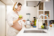 © Drobot Dean - White pregnant woman in headphones making smoothy at home
