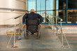 Man wearing jacket riding in wheelchair on ramp by building