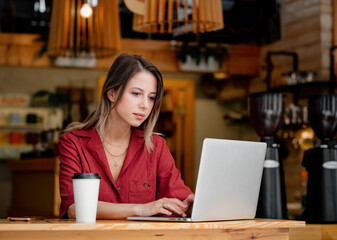 Wall Mural - young woman using laptop computer drink a coffee sits at table in a cafe