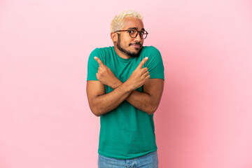 Poster - Young Colombian handsome man isolated on pink background pointing to the laterals having doubts