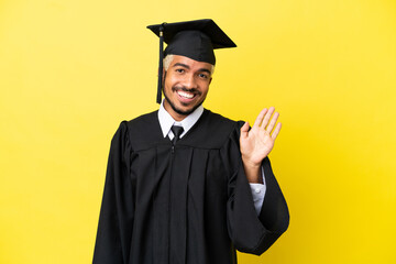 Wall Mural - Young university graduate Colombian man isolated on yellow background saluting with hand with happy expression