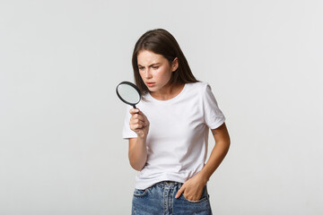 Wall Mural - Serious-looking smart beautiful girl looking through magnifying glass down, searching for something