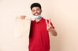 © luismolinero - Young man holding a takeaway food bag ___ smiling and showing victory sign