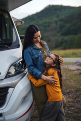 Wall Mural - Mother with small daughter hugging by car outdoors in campsite at dusk, caravan family holiday trip.