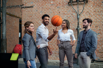 Wall Mural - Group of cheerful young businesspeople playing basketball in office, teambuilding concept.