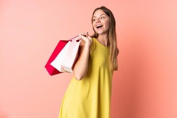 Young Lithuanian woman isolated on pink background holding shopping bags and smiling